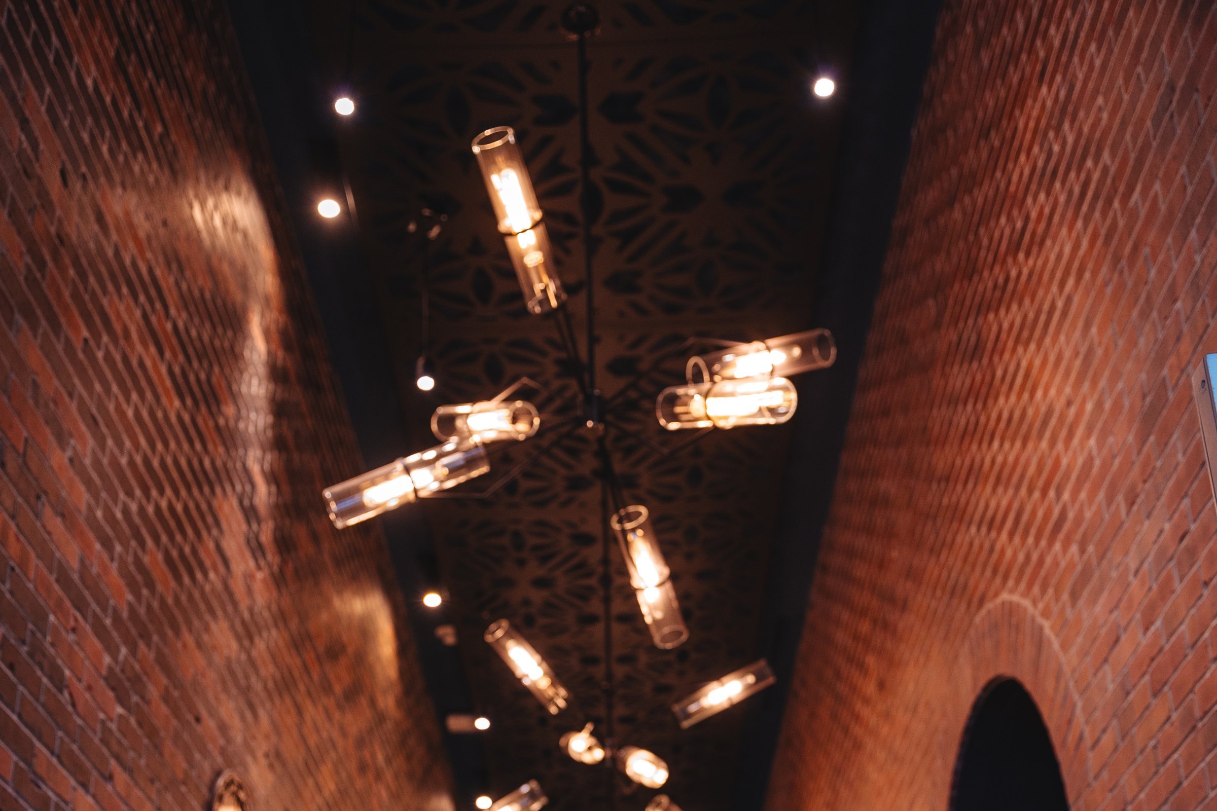 Looking up a narrow brick corridor at a chandelier of glass cylinder lamps