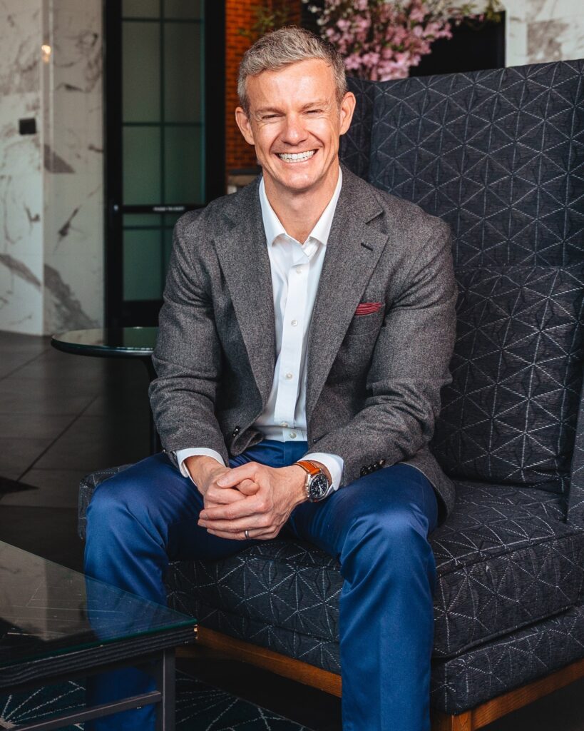 Eric McClerren seated in a grey jacket, hands clasped, smiling